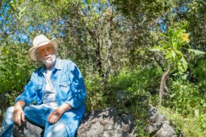 Senior cowboy sitting in the wood resting after activity smoking a cigarette.